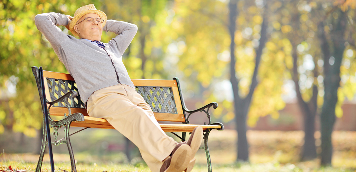 Uomo anziano seduto comodamente su una panchina in un parco, rilassato e sorridente
