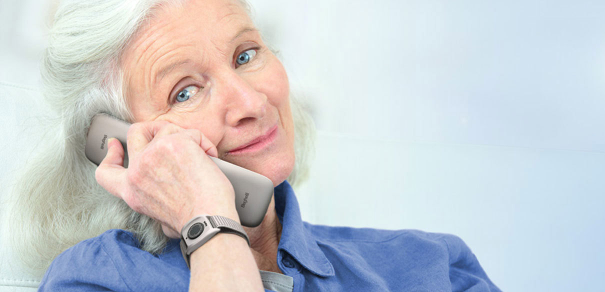 Immagine che ritrae una donna anziana intenta a fare una chiamata con Salvalavita Phone e al polso ha il Salvalavita Band